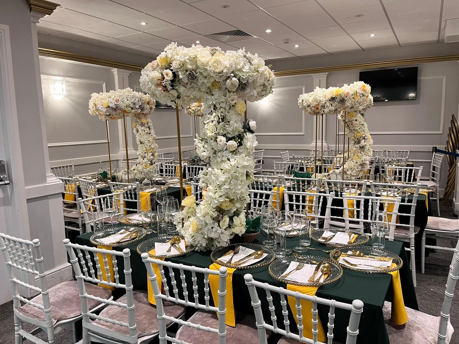 Tall white floral stand centrepieces and gold-rimmed plates on dark green linen